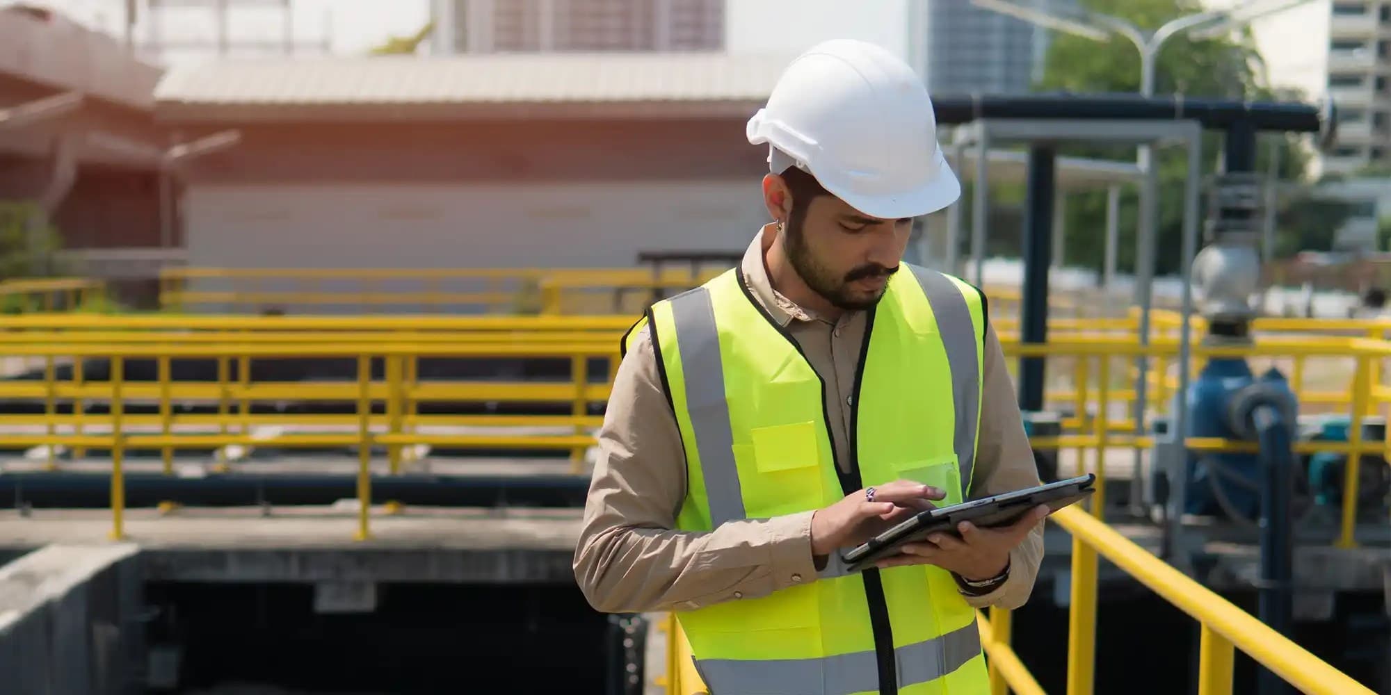 a male worker wearing safety west and helmet looking at a tablet