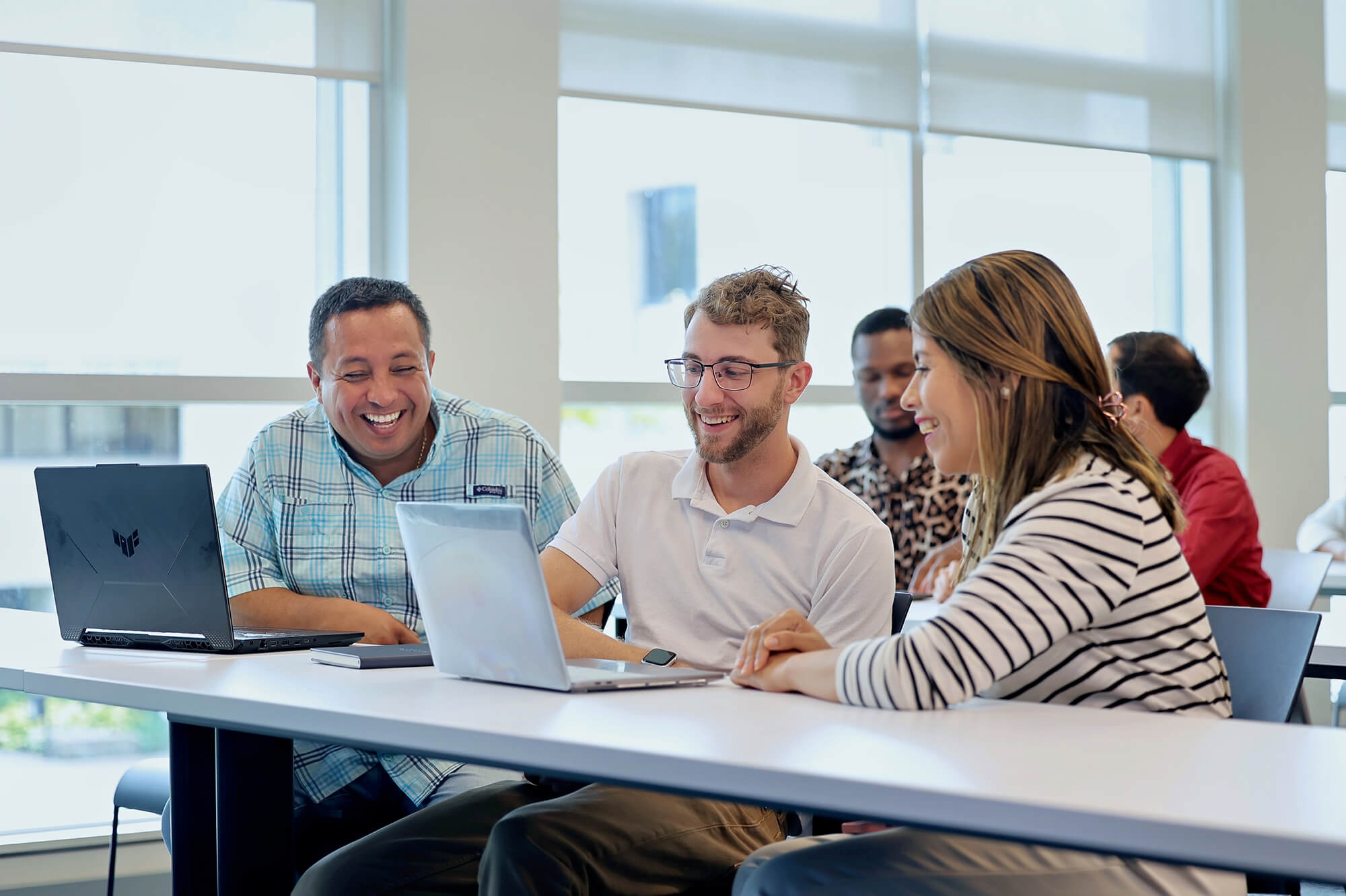 A group of diverse individuals with laptops having a cheerful conversation in a classroom setting