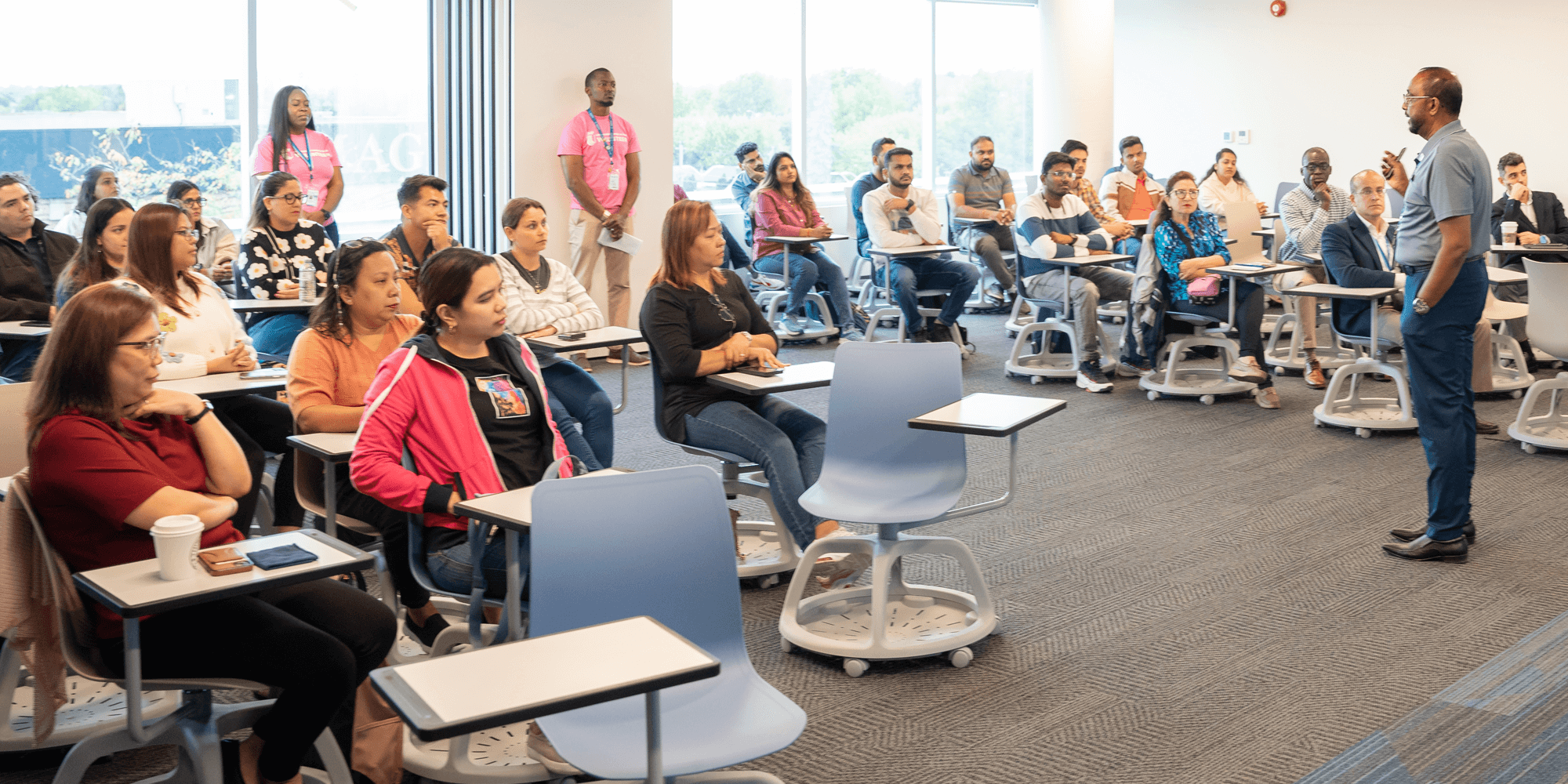 A teacher stands at the front of a classroom, addressing a group of attentive students seated at their desks