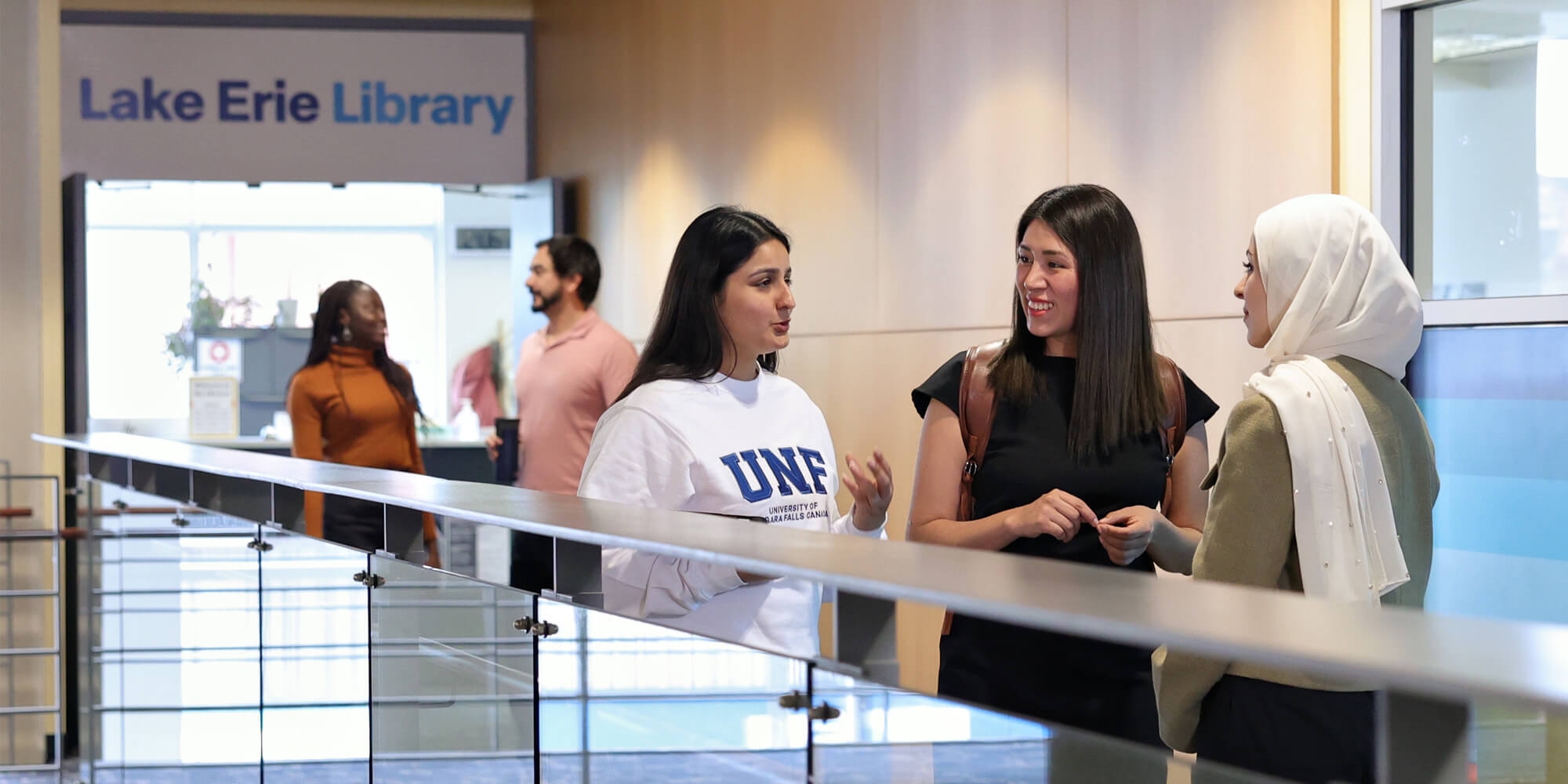 A group of three female students engaged in a cheerful discussion in the UNFC hallway