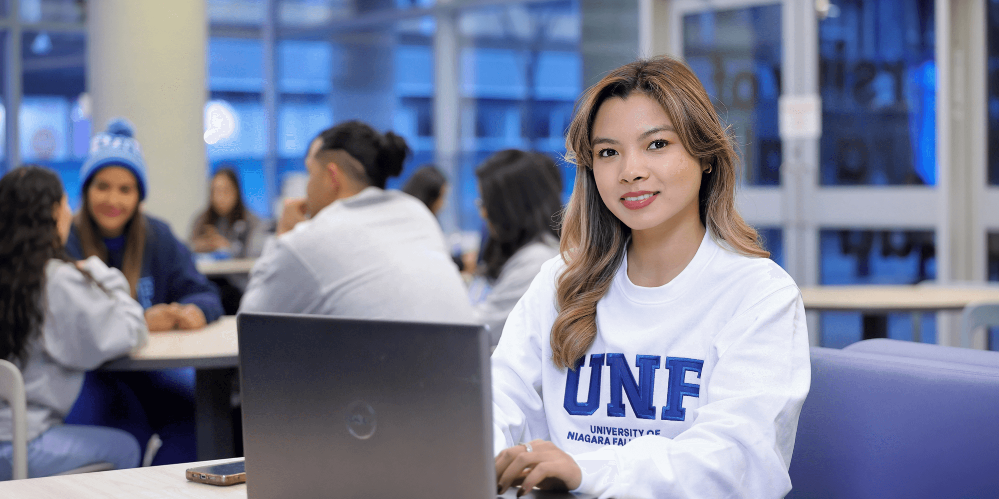 A female student with a laptop sitting at the cafeteria looking at the camera