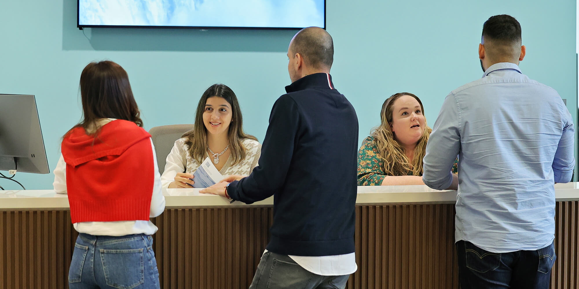 A group of individuals talking to two receptionists at a reception area