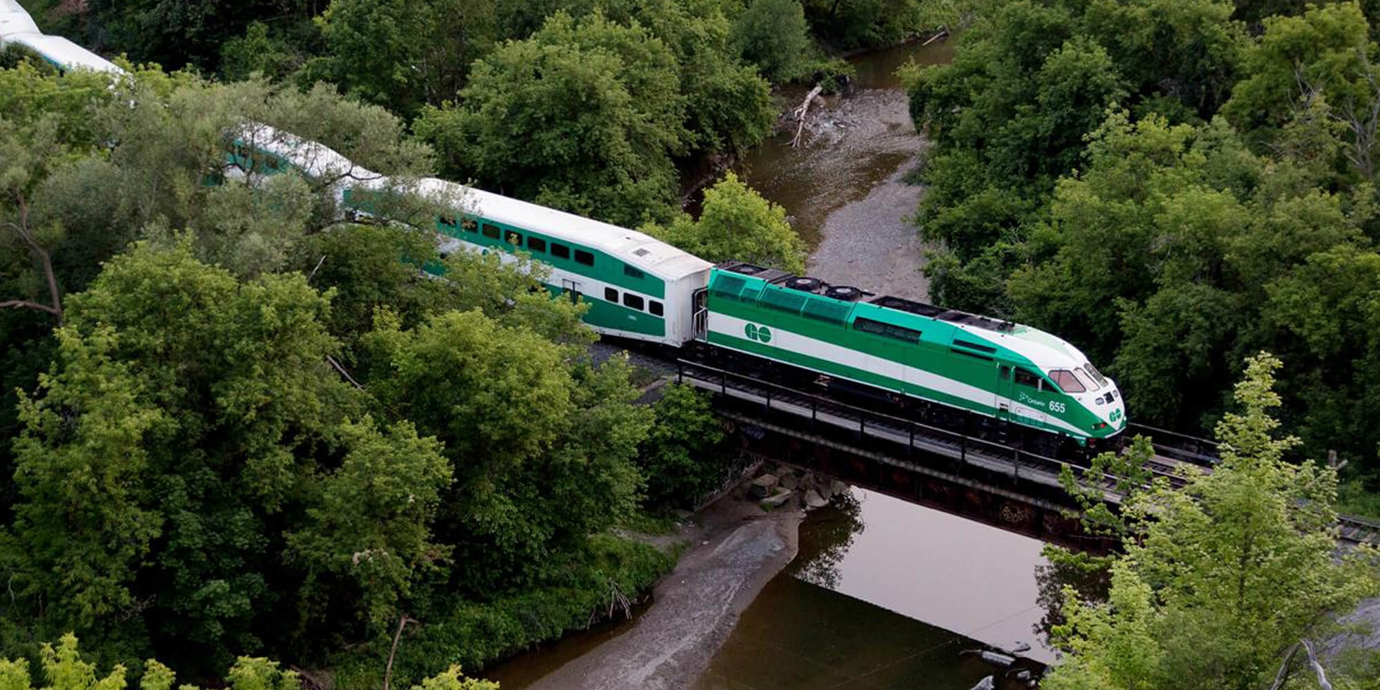 A green and white train crosses a bridge, showcasing its vibrant colors against the scenic backdrop