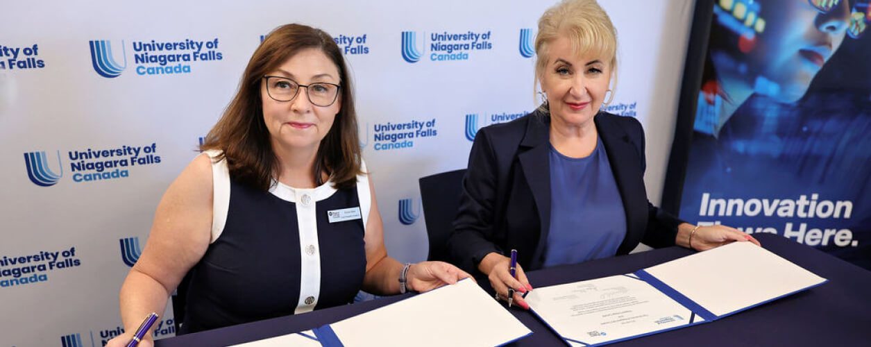 Two women engaged in signing documents at a table, set against a blue background