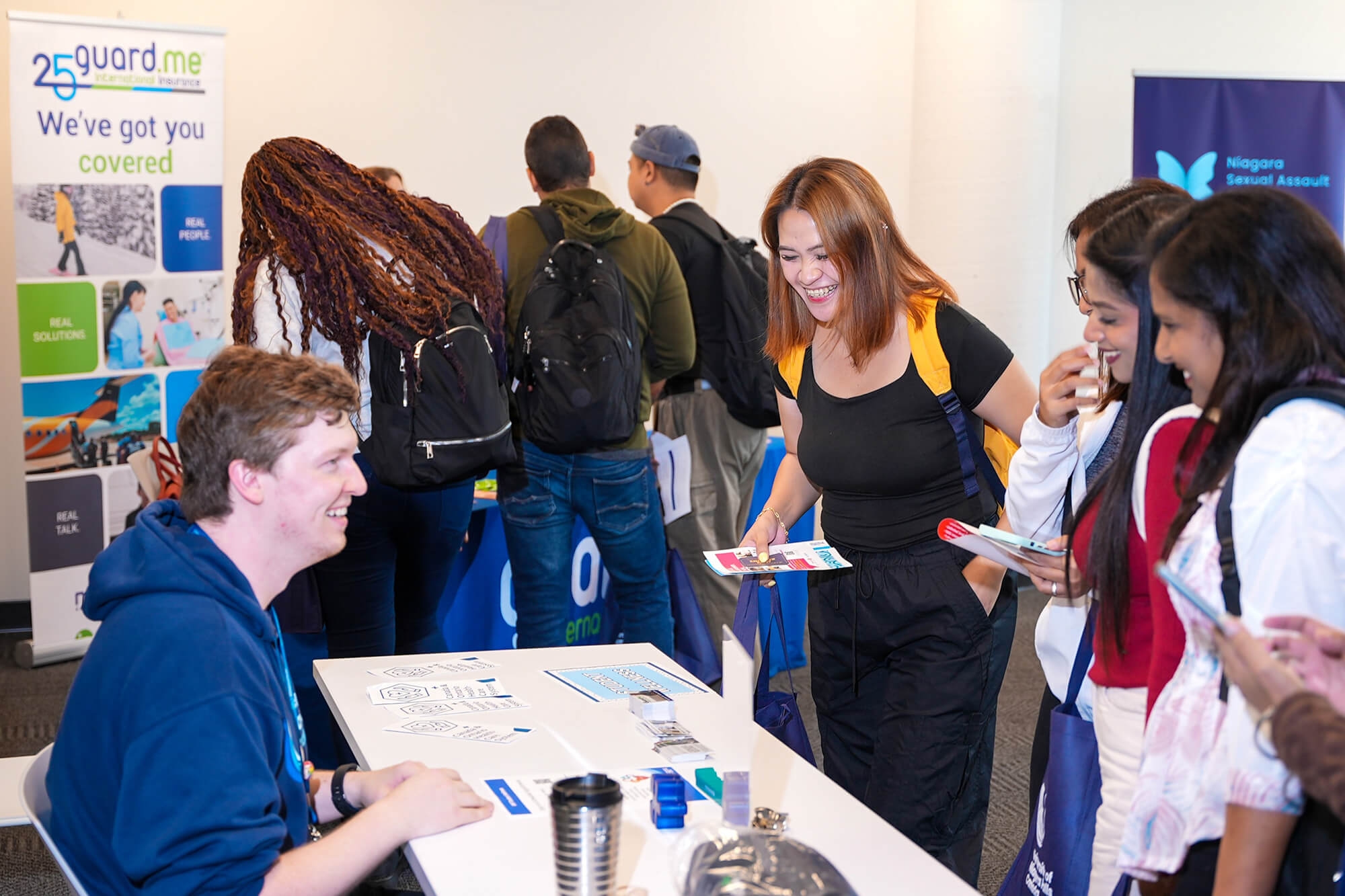 A diverse group of individuals gathered around a table displaying a sign, engaged in conversation and collaboration
