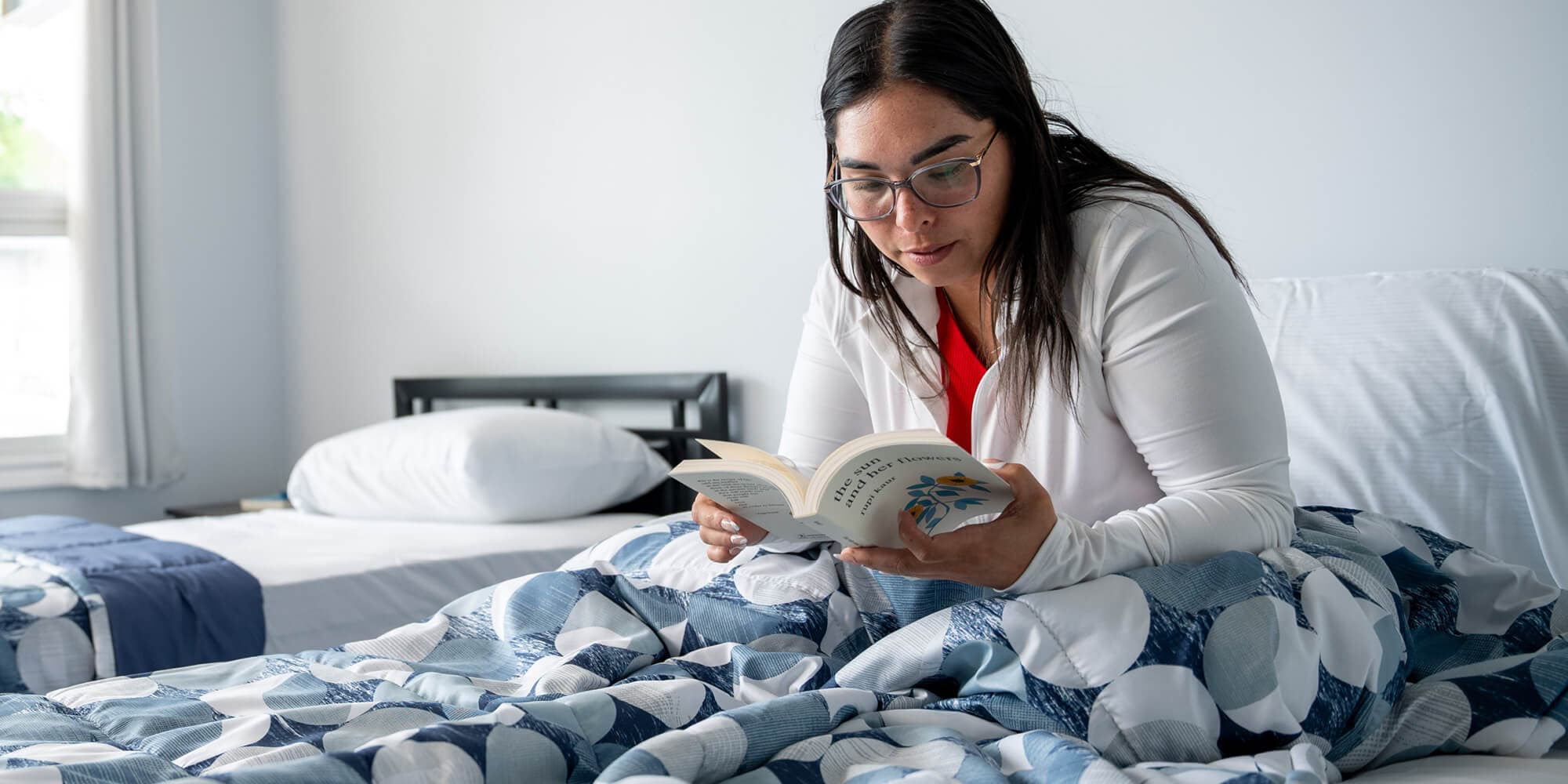 A woman sits on her bed, engrossed in reading a book, surrounded by a cozy atmosphere