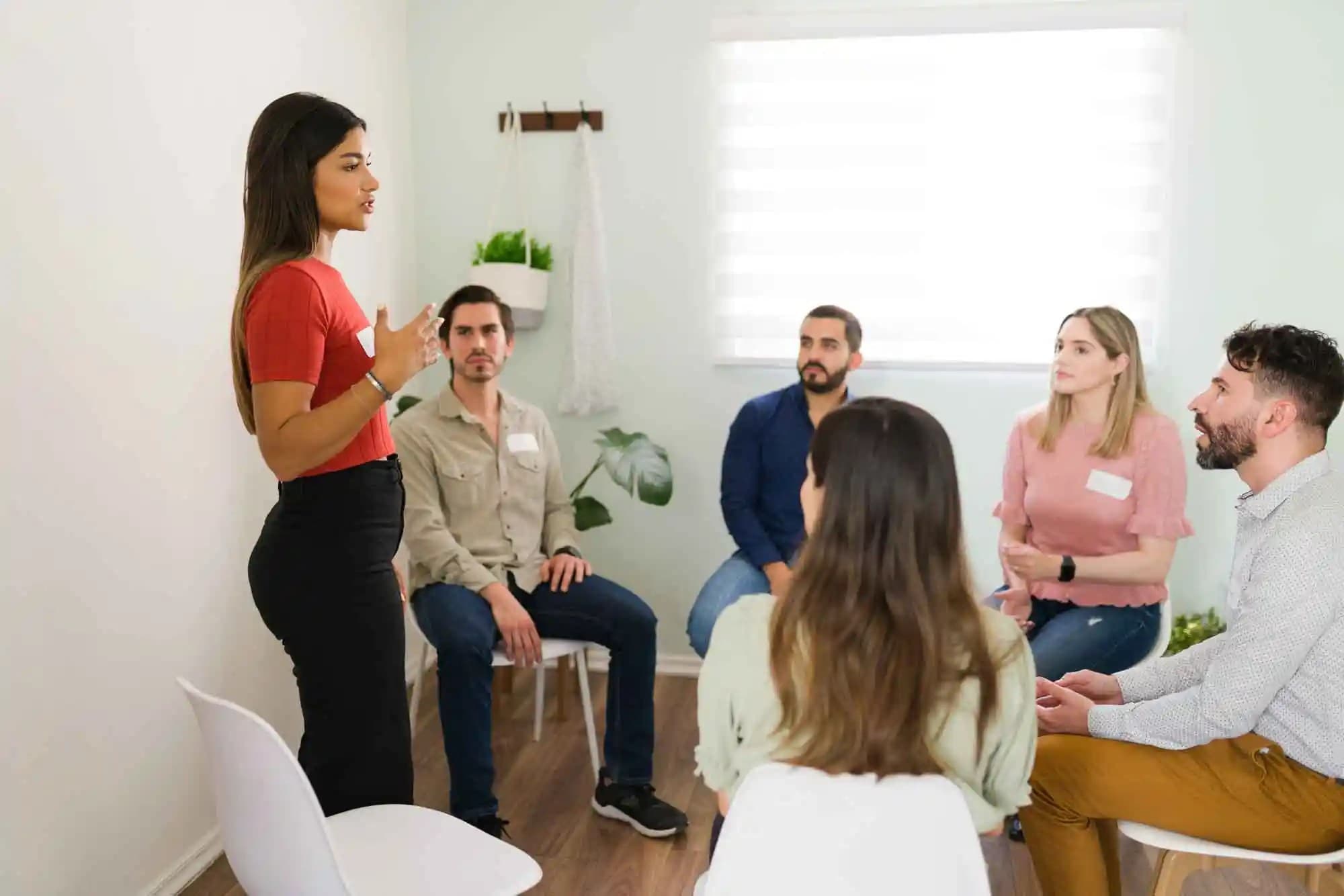 Latin woman standing up to share her experience with young member attending a group counseling.