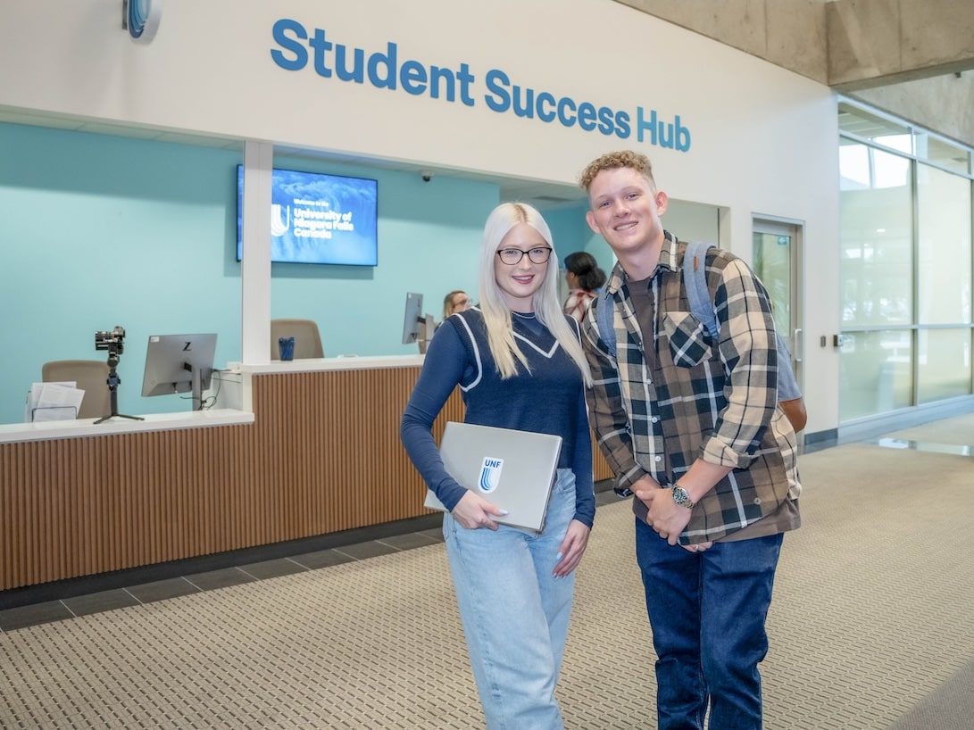 Two young people pose in front of a sign that states "Student Success Hub".