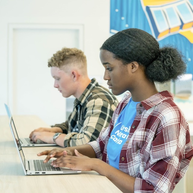 Two students focused on laptops, collaborating on a project in a classroom