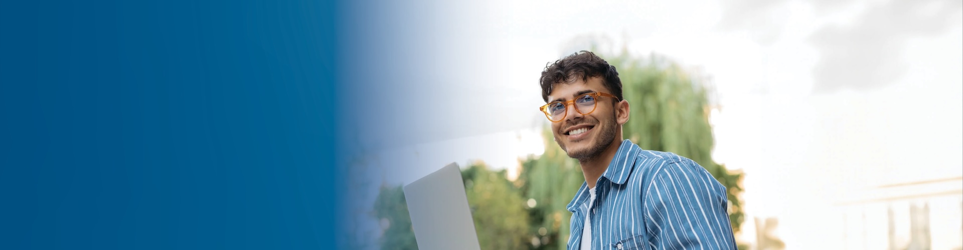 A man in glasses smiling while holding a laptop