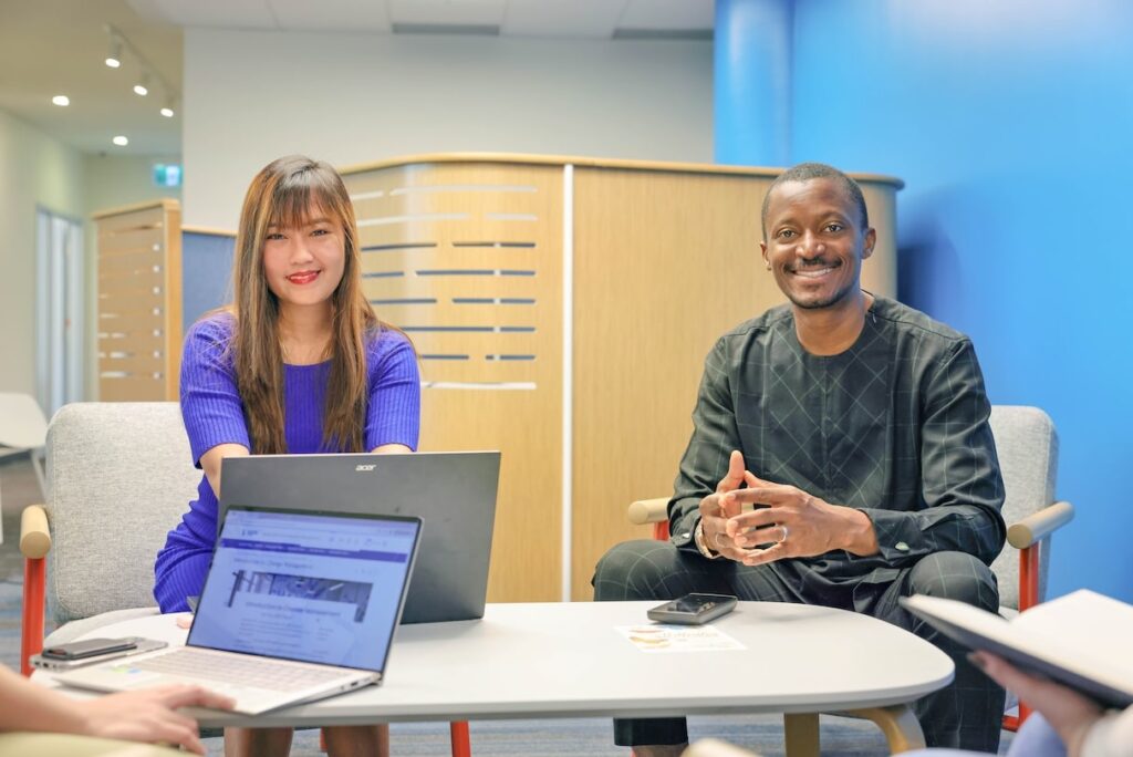 Two individuals seated at a table, each using a laptop, engaged in a collaborative work session.