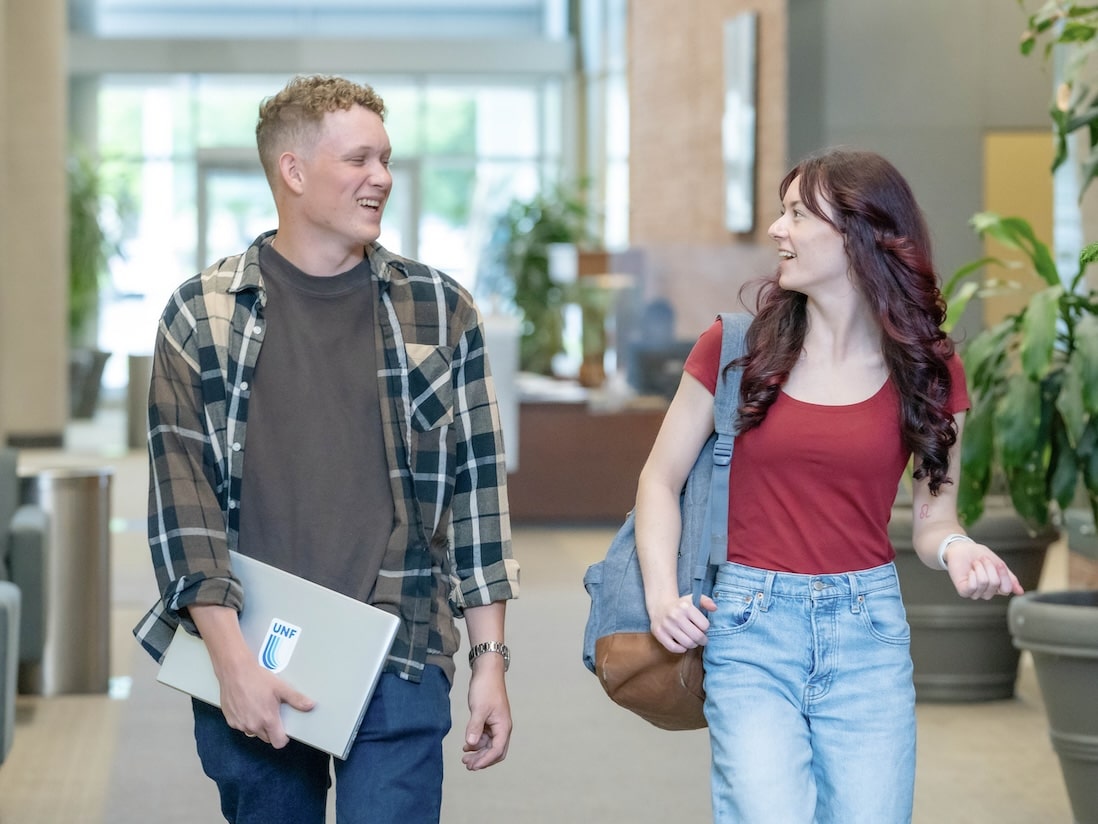 Two students walking side by side in a school hallway, engaged in conversation and carrying their books.