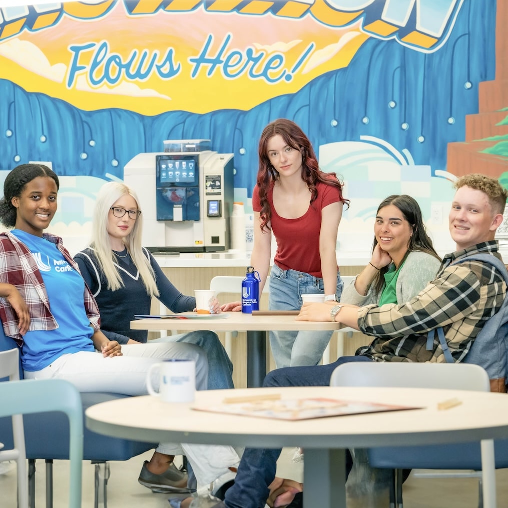 A group of students sitting around a table in front of a mural.