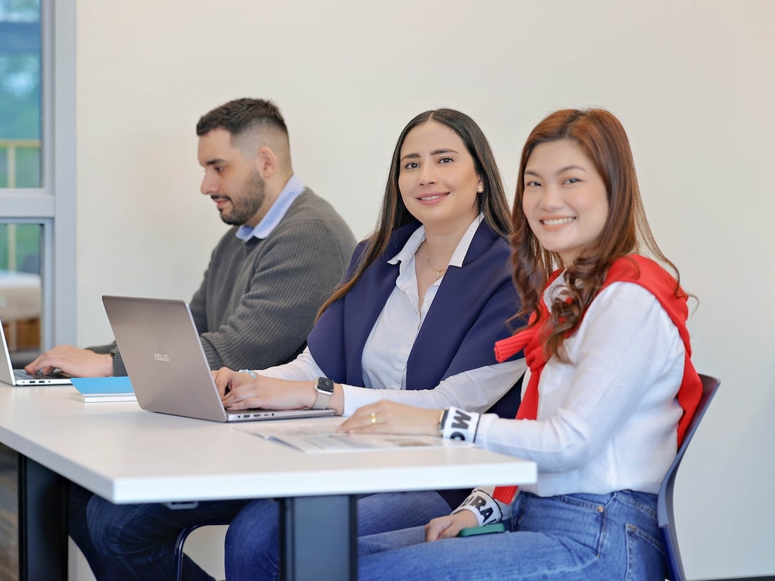 A diverse group of individuals sitting at a table with laptops, engaged in a meeting