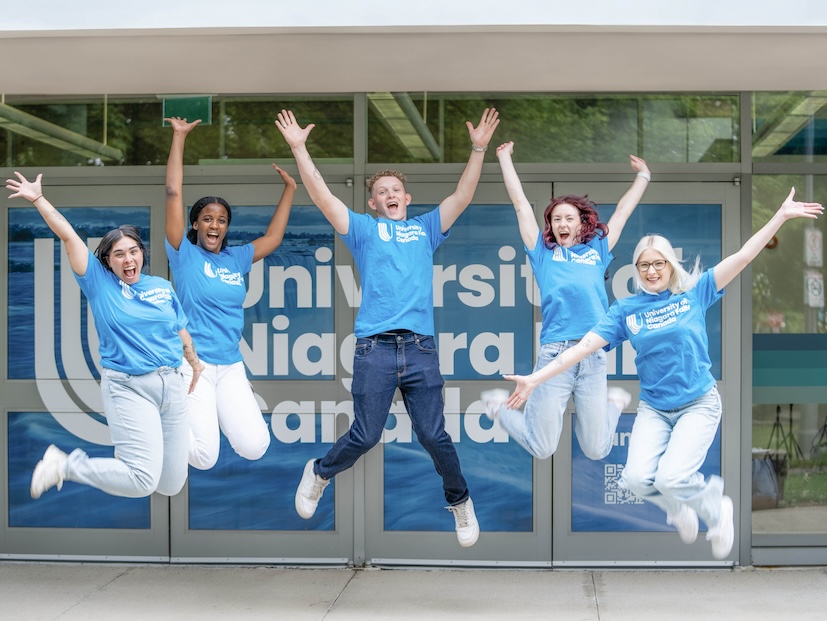 Five young people wearing blue shirts happily jumping in the air.