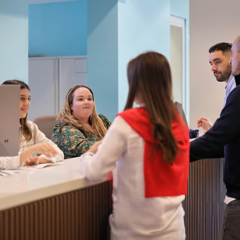 Several people standing near a reception desk, interacting and discussing