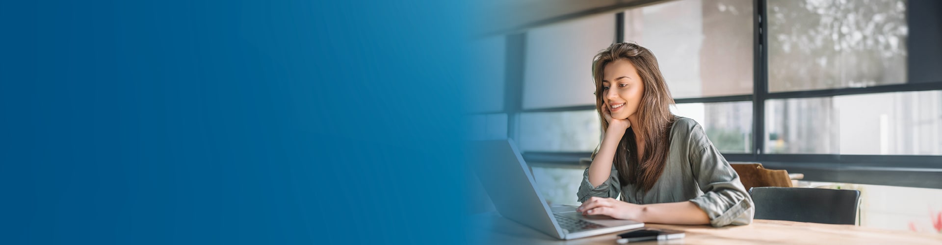 A woman seated at a table, focused on her laptop