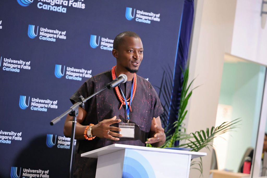 A man stands at a podium, addressing an audience against a backdrop of a blue wall