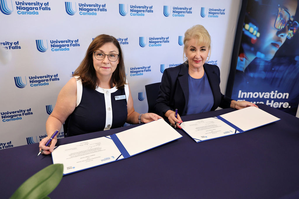 Two women seated at a table, engaged in signing documents, showcasing collaboration and professionalism