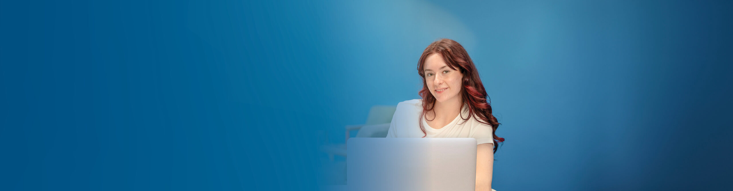 A woman seated at a desk, focused on her laptop