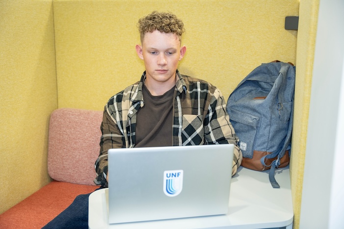 young man seated at a desk, focused on his laptop computer, engaged in study.