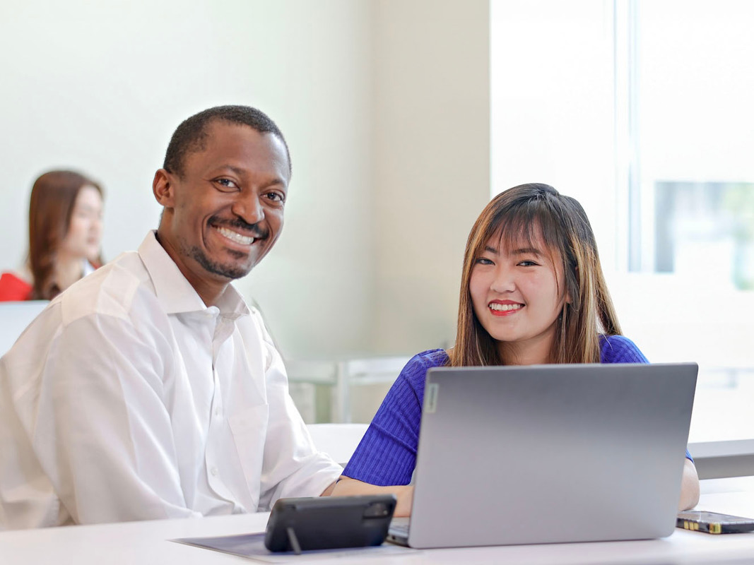 A man and woman are seated at a table, engaged with a laptop in front of them