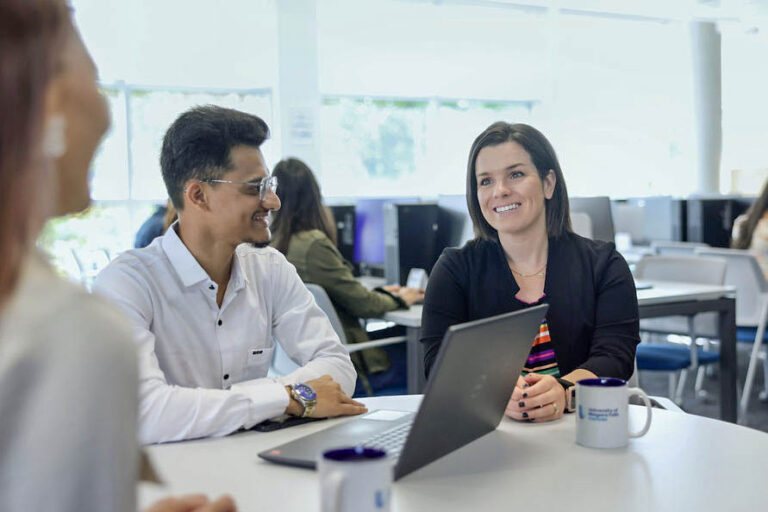 Three colleagues gathered around a table, each with a laptop, working together on a project.