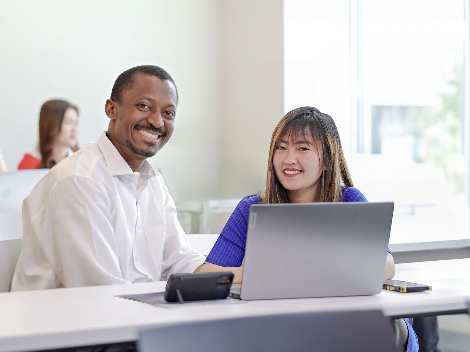 A man and woman are seated at a table, engaged with a laptop in front of them