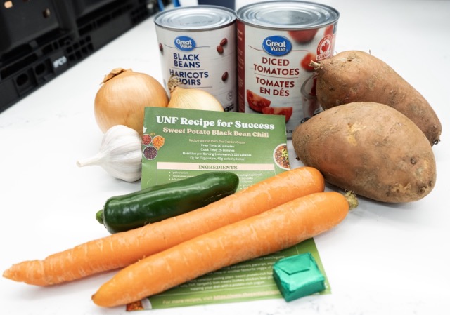 A can of beans alongside fresh carrots, onions, and potatoes