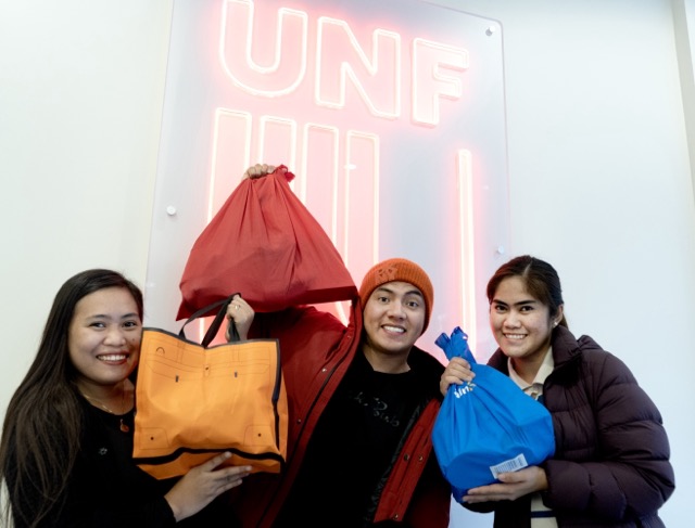 Three people stand together, each holding bags