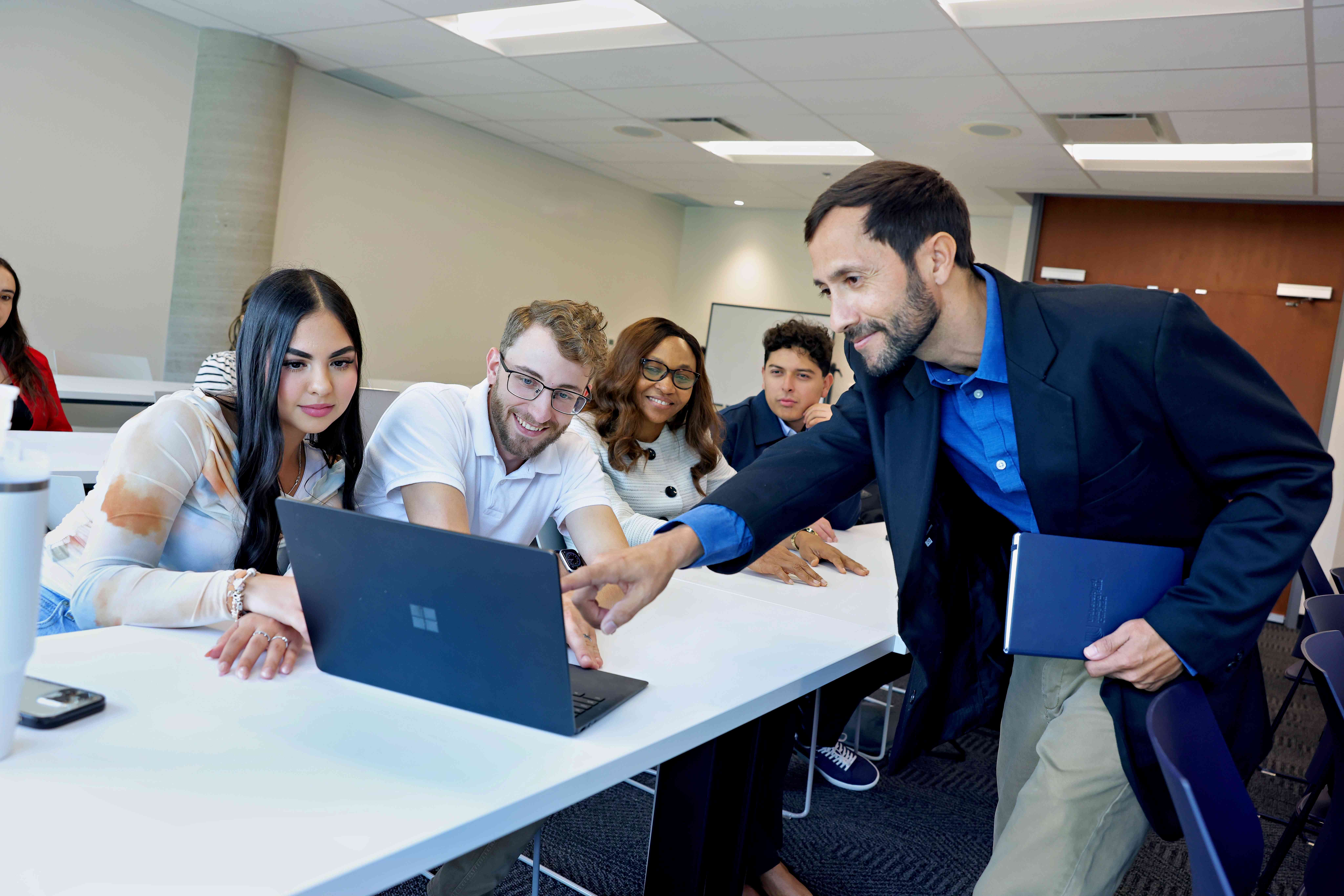 Two women engaged in work, sitting at a table with laptops,A man assists a group of individuals in a classroom setting, fostering a collaborative learning environment. focused on their tasks in a collaborative environment.